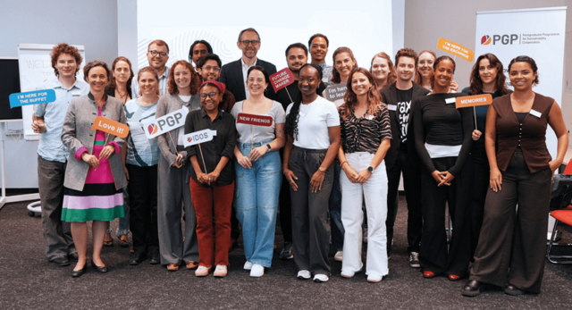 Gruppenaufnahme von Teilnehmenden des Postgraduierten‑Programms, die in einem Seminarraum zusammenstehen und Schilder mit positiven Botschaften zum Programm halten. 